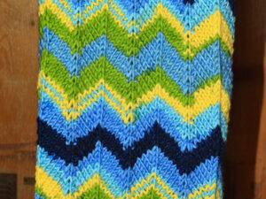 Blue, Yellow and green chunky scarf. A long and warm bright scarf designed and hand knitted by Carole Wareing of Colin and Carole’s Creations and The Wool Boat. This is an adult sized garment, knitted from a chunky yarn, with a chevron pattern in shades of Blue, Yellow and Green. It is ideal for keeping warm on a windy winter’s day whilst doing some gardening, locking, bicycling, standing markets, fishing, watching outdoor sports and events, or walking and rambling. The garment is approx 72 inch long and 11 inches wide. The scarf is for sale for £25 from the Wool Boat The warmer is knitted from J C Bretts “Party Time” chunky knitting acrylic yarn Shade PT 2 which has bold Blue, Yellow and green shades in it. The yarn knits to most chunky knitting patterns and is available from the Wool Boat of which we have a range of 7 other shades at £3.50 per 100 gram ball. Posted out would be for £30 including delivery to a uk address, Copyright Colin Wareing Garment 522 Cw 7707