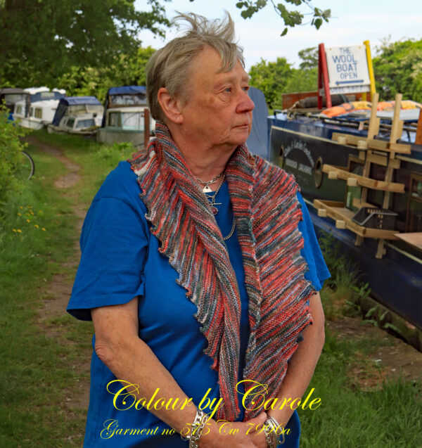 Carole models a red and grey Stonewash shawl Carole, the knitter shows off a dragon tooth shawl she has hand knitted aboard the narrow boat “Emma Maye” in Lancashire by Carole Wareing of Colin and Carole’s Creations. This exclusive garment is an adult sized shawl, knitted from a yarn available from The Wool Boat which is produced by James C Brett. The yarn used for this shawl is an acrylic yarn from the James C Brett’s “Stonewash” range, shade SW1. The colours are shades of Red and grey The stitches used to create this shawl have produced a textured structure to the garment. The yarn is an acrylic one, very warm and snuggly and easy maintaince. The shawl is approximately 72 inch long and 11 inch deep at its widest point and has about 64 dragon’s teeth.