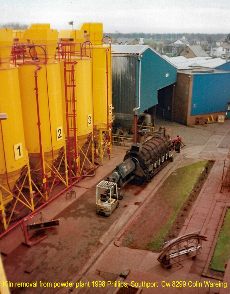 Kiln removal from powder plant 1998 Philips, Southport.                          Cw 8298 
A Elino kiln is removed from the Powder plant at the Philips, the old Mullard’s factory in Crossens near Southport.
This kiln is being removed by specialist contractors to make way for a new spray drier. 
To the right of this picture are the big yellow silo’s that the raw materials were stored in, of iron oxide, zinc, manganese which arrived on to the site either in bulk bag, tankers or containers.
The powder plant produced a metal powder that was pressed into shapes that were fired in kilns to produce magnets to fit around the tube in a cathode ray tube television.
The basic process of the powder plant was to mix powders together, roll them up into little balls, fire them through a rotary kiln at about 1200C, this was known as the “Dry Process”
The balls where then allowed to cool before being ground down in a ball mill with water in them to form a slurry, “Milling”
A liquid binder was added to the slurry and it was spray dried to form the finished powder which was either used on in the factory at Crossens or exported to such places as Taiwan.  “Spray Drying”
As the slurry was spray dried the evaporating water was let off as steam, through a scrubber that for most of the time collected any powder granules within the steam. 
Not quite sure of the date but probably about 1998
The plant closed at the end of 2003, with the work going to Poland and China.
I worked in the factory from 1987 to 2003, working in the powder plant from 1987 to 1992 as a operator, a couple of years making magnets then from April 1994 until the powder plant closed in December 2003 I was a group or shift leader in the powder plant. 
Colin Wareing 16.5.2023
Cw 8298 Colin Wareing
 Image Cw 8298 copyright Colin Wareing of Colin and Carole’s Creations
