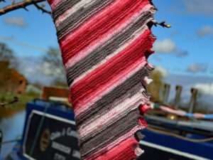 Red and grey shades Dragon tooth Shawl A contrasting shades Dragon tooth shawl hand knitted aboard the narrow boat “Emma Maye” in Lancashire by Carole Wareing of Colin and Carole’s Creations. This unique garment is an adult sized shawl knitted from a yarn from a visit to another yarn shop, other than The Wool Boat. The garment is created from a yarn with bright shades of Reds, pinks, and greys. The shawl is 72 inch or 180cm long and 12 inch or 30cm deep at its widest point and has about 63 dragon’s teeth. The yarn is an acrylic one, so easy care.