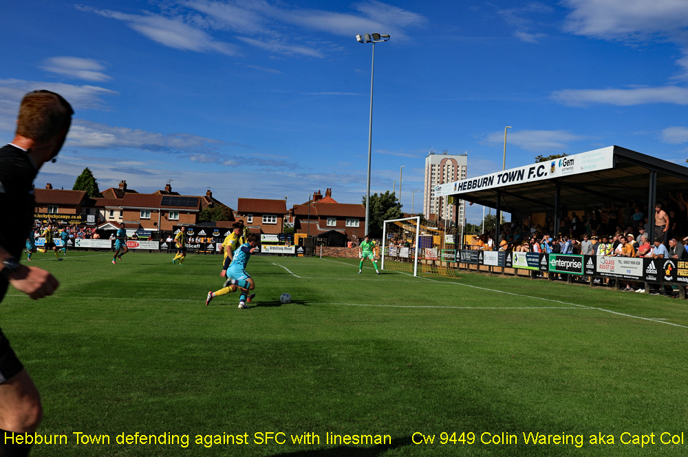 Hebburn Town defending against SFC with linesman

Hebburn Town F C are defending their goal against a Southport F C attack as the linesman tries to keep up, on Saturday the 8.8.2026 in the first game Hebburn have played in the National League North. 
Hebburn had won promotion from the Northern Premier league at the end of last season, to the highest league they have played in in the English football pyramid. 
They went on to make a winning start to life at this level winning this game 3-1.
Hebburn are the team in the yellow and black shirts while Southport are in their away kit of blue.
This scene is due to change in the next few years with the planned demolition of the tall block of flats behind the ground.
Image Cw 9449 copyright Colin Wareing of Colin and Carole’s Creations
