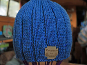 Denim Blue Aran Beanie Hat A denim blue adult Aran Beanie hat hand knitted aboard the narrow boat “Emma Maye” in Lancashire by Carole Wareing of Colin and Carole’s Creations. Great for an adult or teenager, Colour – shade of denim blue. British Wool, reared, sheared, spun and hand knitted in Britain. Machine washable at 40 degrees C on a gentle wool or wash cycle. The price is £15 or can be posted to a UK address with p and p if applicable. Created from a shade West Yorkshire Spinners yarn “Colour Lab Aran” range which we stock on The Wool Boat. Hand knitted by Carole Wareing Garment 772 Cw 9471