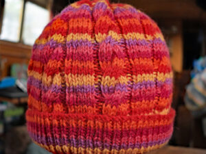 Cabled Tutti Frutti adults’ hat in shades of red and orange. A red and orange adult cabled hat hand knitted aboard the narrow boat “Emma Maye” in Lancashire by Carole Wareing of Colin and Carole’s Creations. Great for an adult or teenager, Colour – shades of red and oranges. British Wool, reared, sheared, spun and hand knitted in Britian. Machine washable at 40 degrees C on a gentle wool or wash cycle. The price is £15 or can be posted to a uk address with p and p if applicable. Created from shade “Tutti Frutti” from West Yorkshire Spinners yarn “Colour Lab DK” which we stock on The Wool Boat. Hand knitted by Carole Wareing Garment 783 Cw 9472
